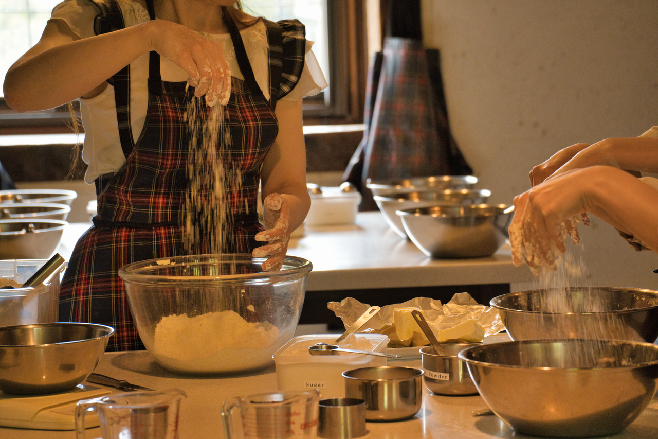 A woman in an apron mixes flour in a kitchen setting, showcasing hands-on cooking.